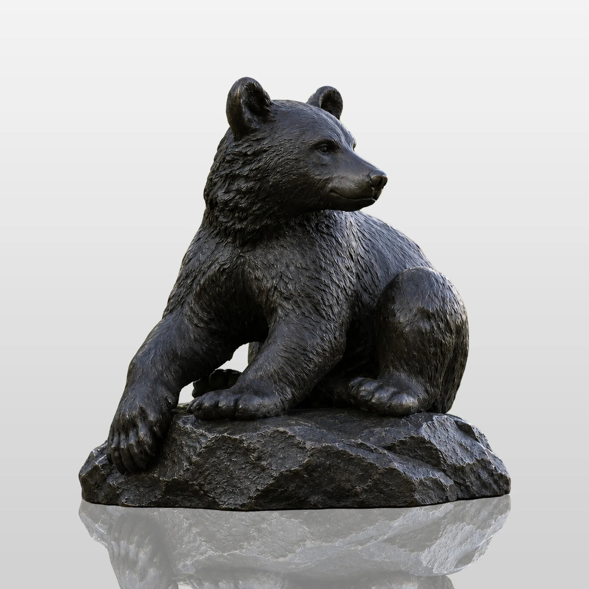 Dark bronze seated bear statue sits on pavement within a green public park.