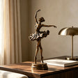 Bronze ballerina table sculpture stands on the wooden desk under soft indoor sunlight.