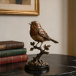 Bronze robin bird table sculpture sits on the black marble table beside stacked hardcover books.