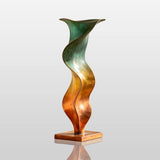 An abstract vase bronze sculpture stands on a wooden cabinet in a sunlit room.