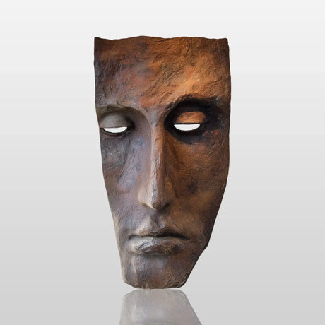 A realistic bronze wall mask sculpture in human face design is mounted on a plain wall in a sunlit modern interior.