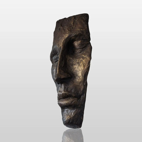 A modern bronze face wall mask sculpture hangs on a light colored wall in a bright, contemporary living room.