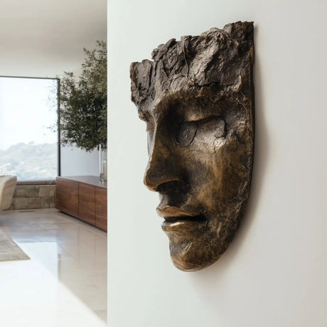 A textured bronze face wall mask sculpture is mounted on a plain white wall in a bright modern home.