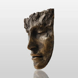 A textured bronze face wall mask sculpture is mounted on a plain white wall in a bright modern home.