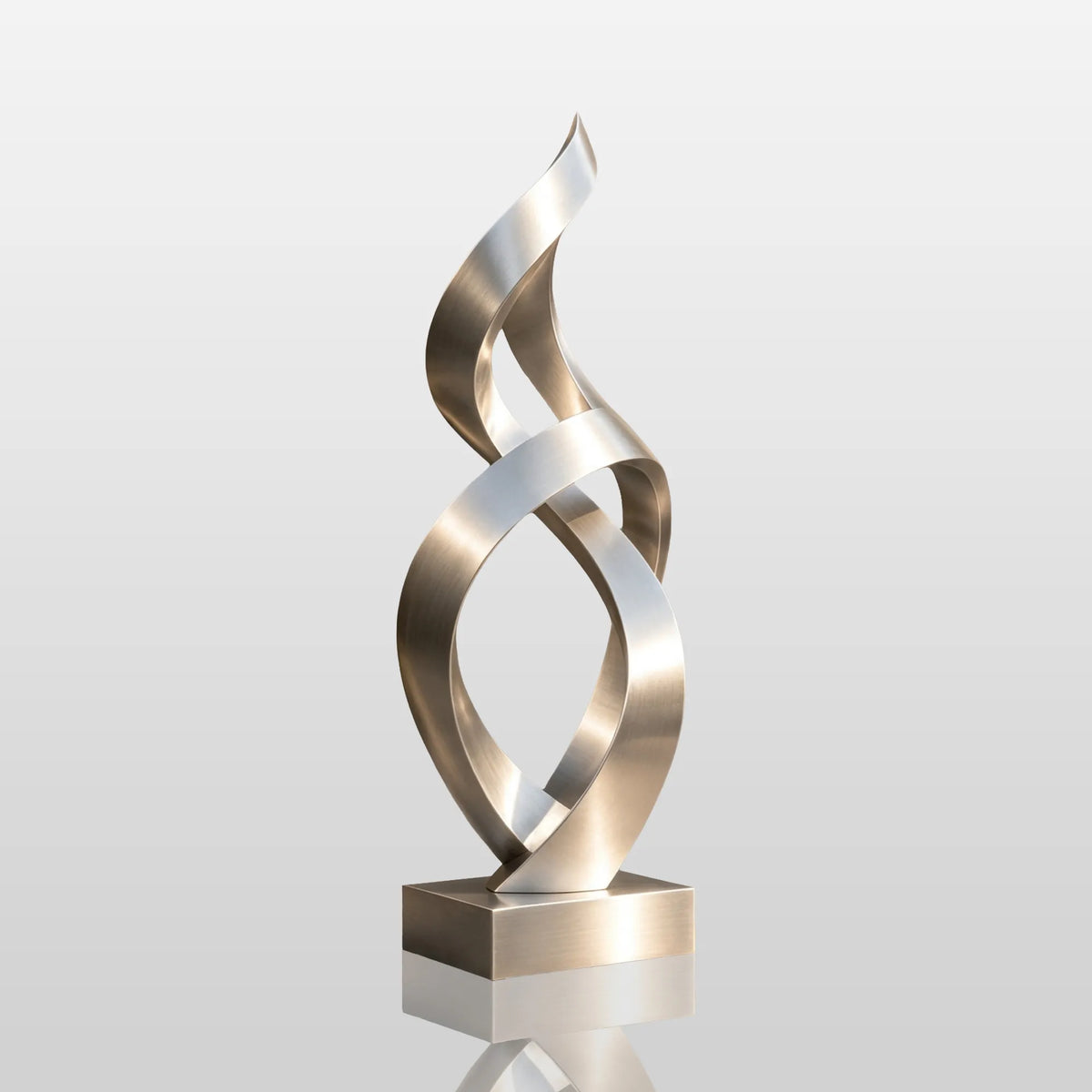 A stainless steel twist sculpture stands on paved ground outside a modern building.