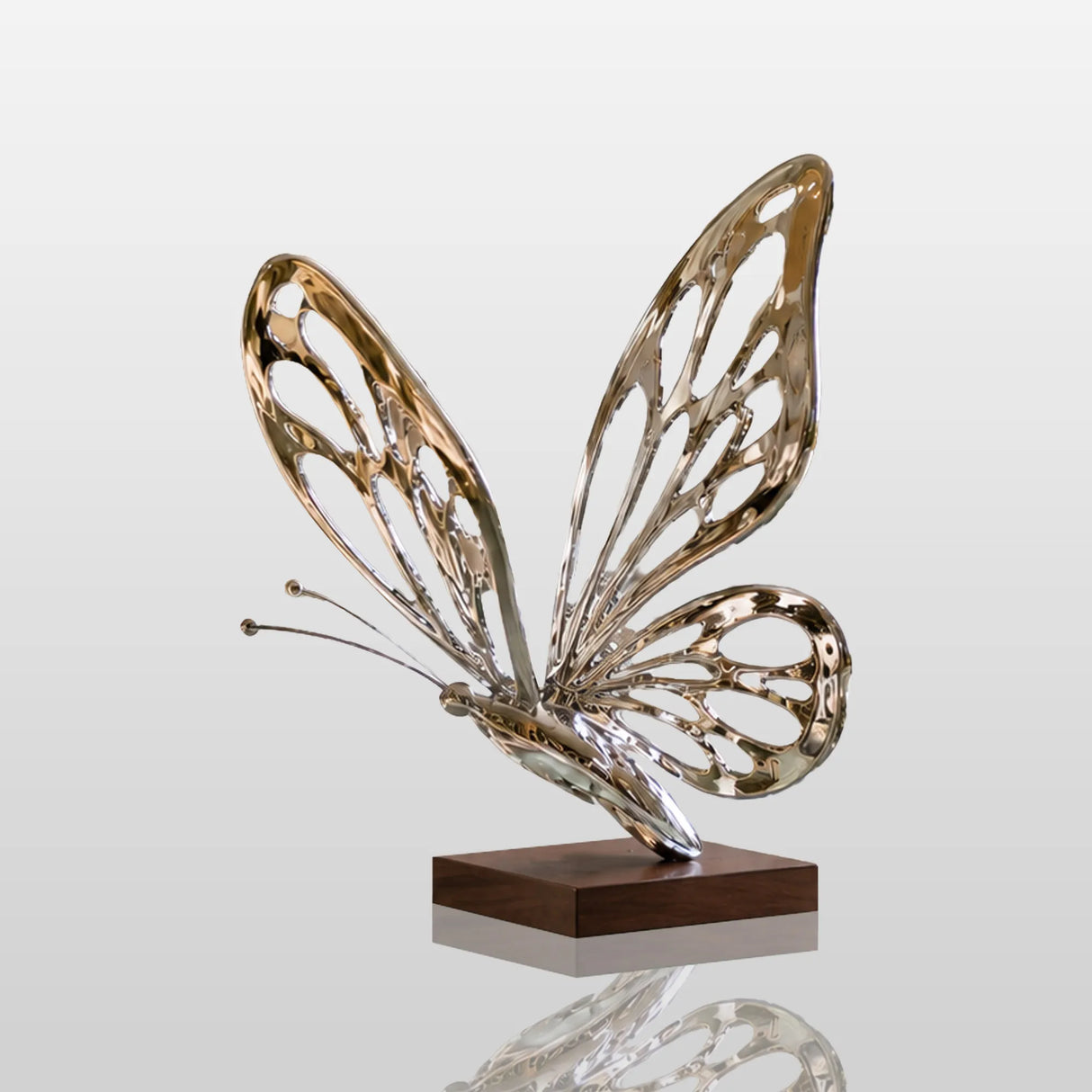 A hollow polished stainless steel butterfly sculpture sits on a curved glass table inside a bright living room.