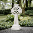 White marble Celtic cross headstone rests on gravel ground surrounded.