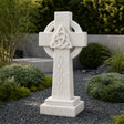 The marble Celtic cross headstone sits on dark gravel among green garden shrubs.