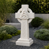 The marble Celtic cross headstone sits on dark gravel among green garden shrubs.