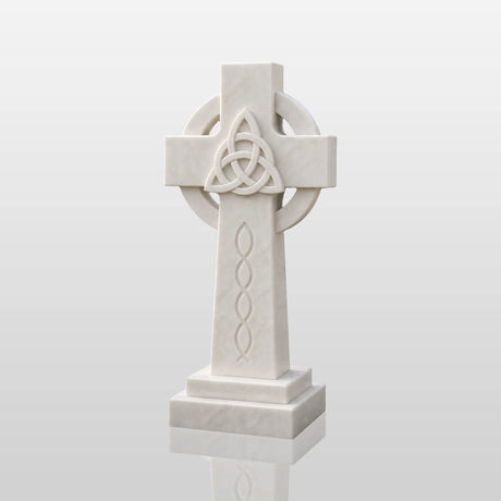 The marble Celtic cross headstone sits on dark gravel among green garden shrubs.