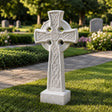 White Celtic cross marble headstone stands on grass beside a pathway.