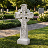 White Celtic cross marble headstone stands on grass beside a pathway.