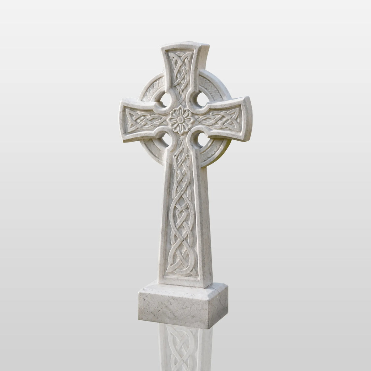 White Celtic cross marble headstone stands on grass beside a pathway.