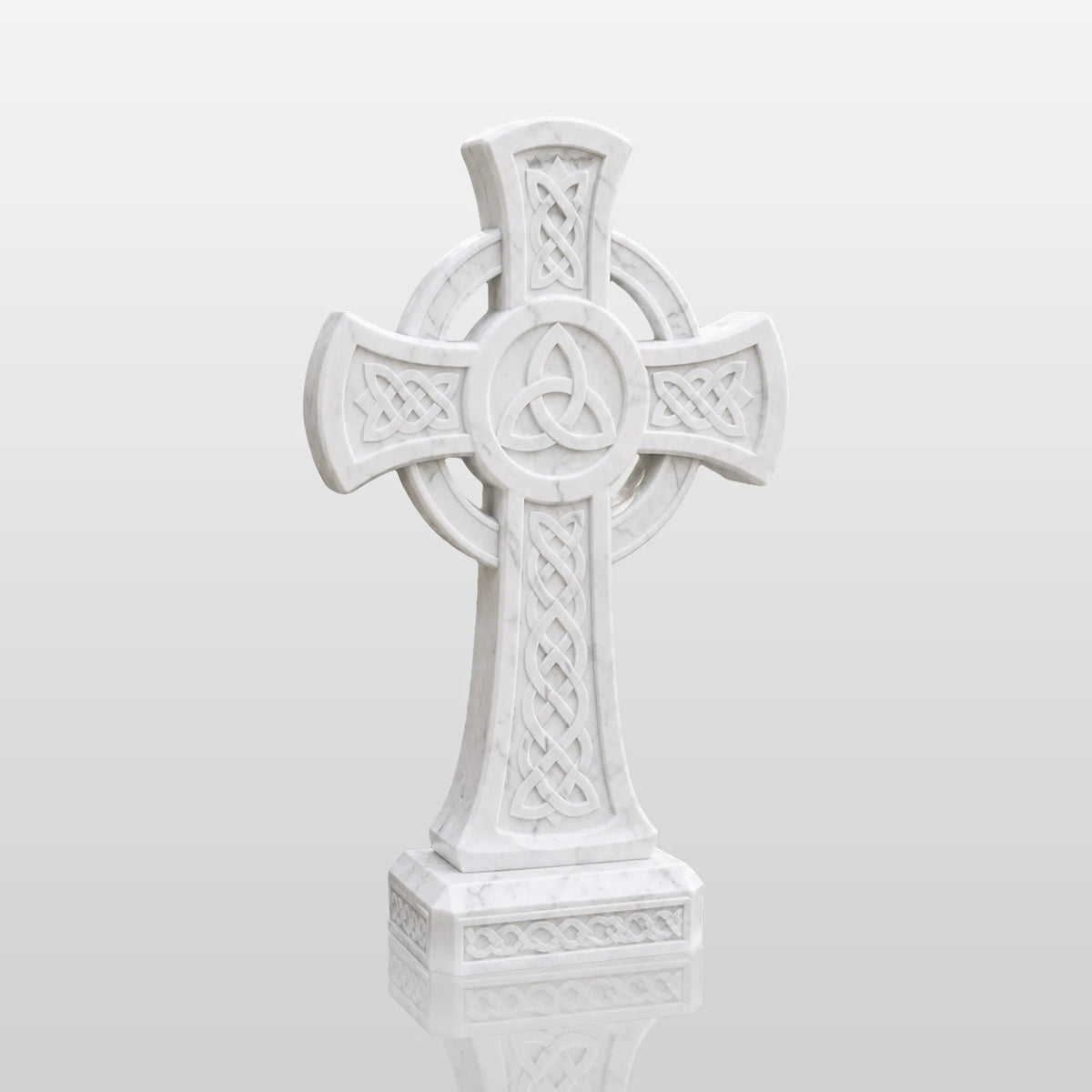 A marble Celtic cross tombstone with triangle knots sits among blooming roses near a church.