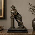 Bronze tabletop sculpture of a neoclassical leaning lady stands on the table indoors.