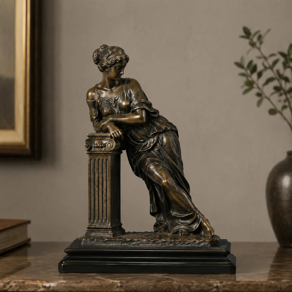 Bronze tabletop sculpture of a neoclassical leaning lady stands on the table indoors.