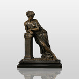 Bronze tabletop sculpture of a neoclassical leaning lady stands on the table indoors.