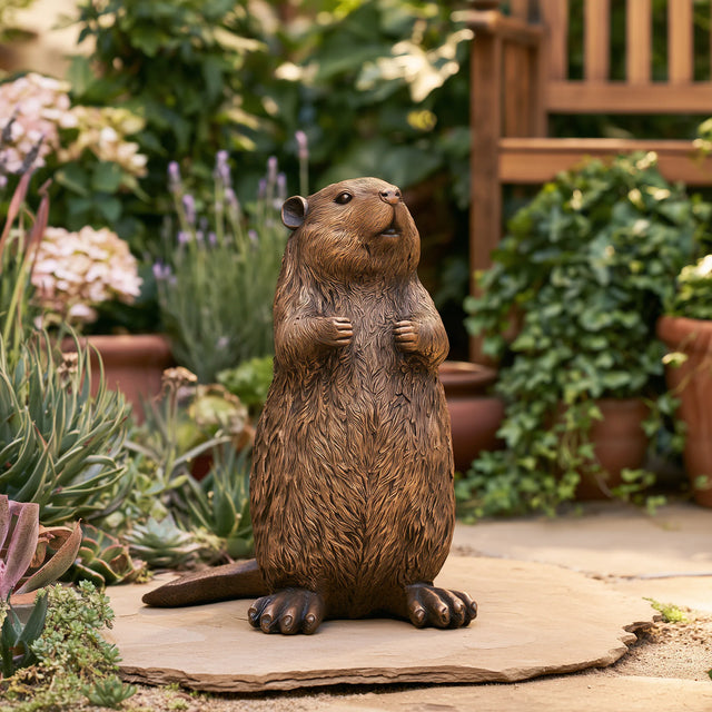 A cute bronze beaver statue stands on the yard surrounded by lush garden plants.