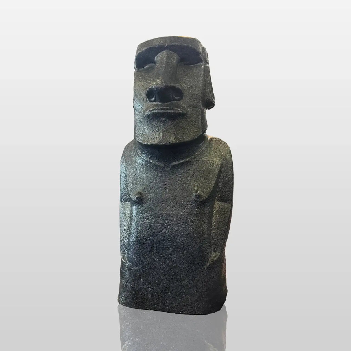 A large textured Moai stone statue rests surrounded by natural rocks inside a minimalist art gallery lit by ceiling spotlights.