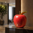 Fiberglass red apple sculpture is displayed on the dark marble table indoors.
