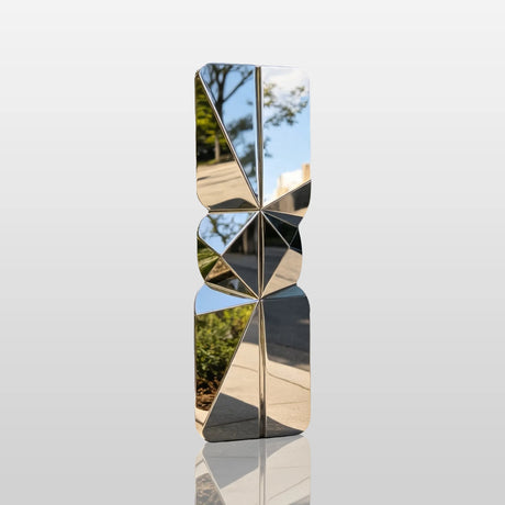 A mirror polished stacked geometric stainless steel sculpture sits on city sidewalk beside modern office building.
