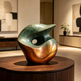 A gradient bronze organic sculpture in organic form stands on a wooden round table inside a modern room.