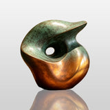 A gradient bronze organic sculpture in organic form stands on a wooden round table inside a modern room.