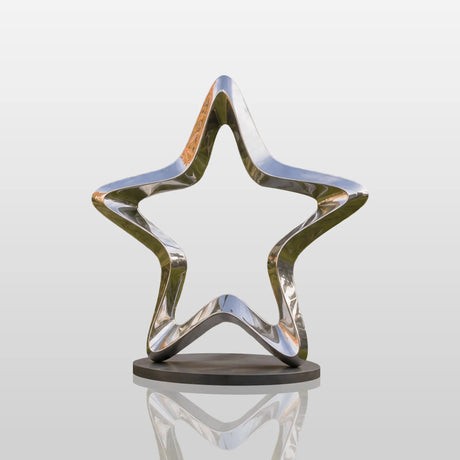 A mirrored stainless steel star sculpture stands on a lawn in front of a luxury house.