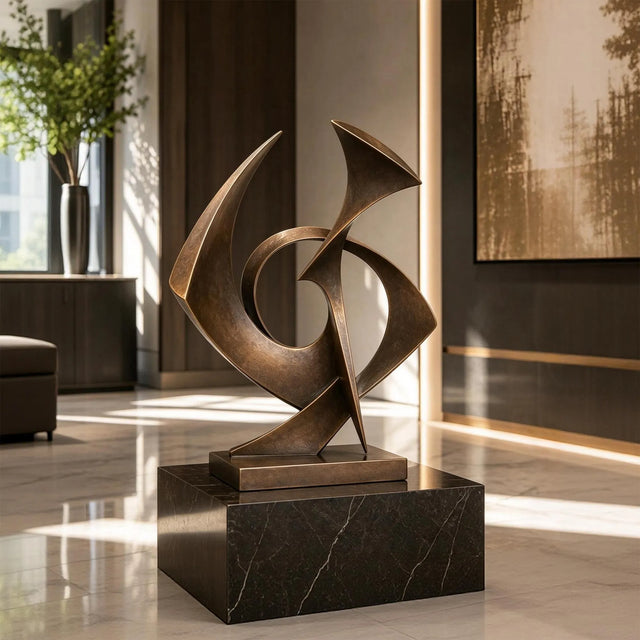A bronze sculpture with intertwined shapes rests on a dark stone base inside a room.