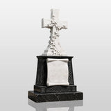 White ivy marble cross headstone with blank scroll plaque sits on black granite base amid gray tombstones in a sunlit cemetery.