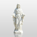 A white marble Jesus statue with open hands stands on the pavement in front of a church entrance.