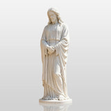 White marble Jesus statue stands on stone pavement beside a church building.