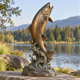 A bronze jumping salmon sculpture on wave rests natural scenery behind it.