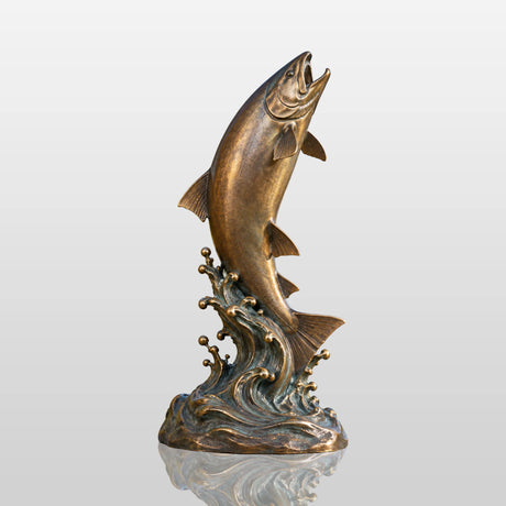 A bronze jumping salmon sculpture on wave rests natural scenery behind it.