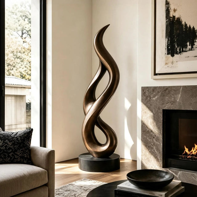A tall twisted bronze sculpture stands in a bright modern living room beside a fireplace.