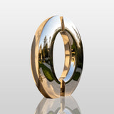 Polished split ring stainless steel sculpture stands on the pavement beside a residential building.