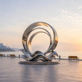 The stainless steel ring wave sculpture stands on the seaside plaza at sunrise.