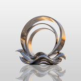 The stainless steel ring wave sculpture stands on the seaside plaza at sunrise.