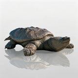 A large bronze turtle statue rests smoothly on beach sand against blue ocean scenery.