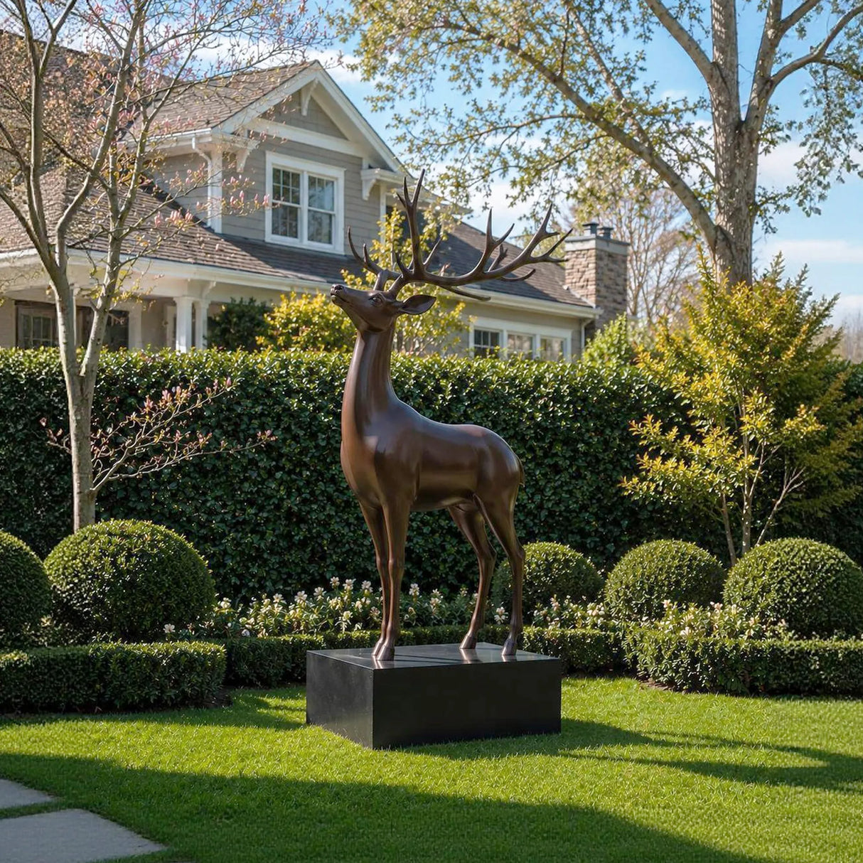 Bronze deer statue stands on the green lawn in front of a residential house.