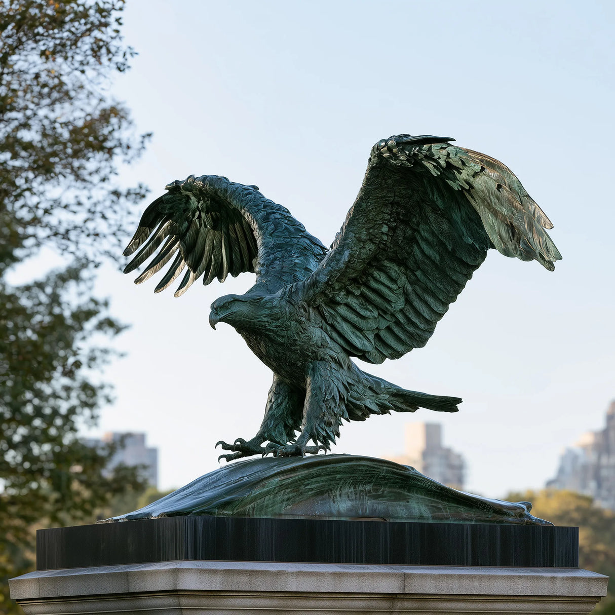 Patinated bronze eagle statue with wide spread wings stands on stone monument in the outdoor public space.