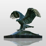 Patinated bronze eagle statue with wide spread wings stands on stone monument in the outdoor public space.