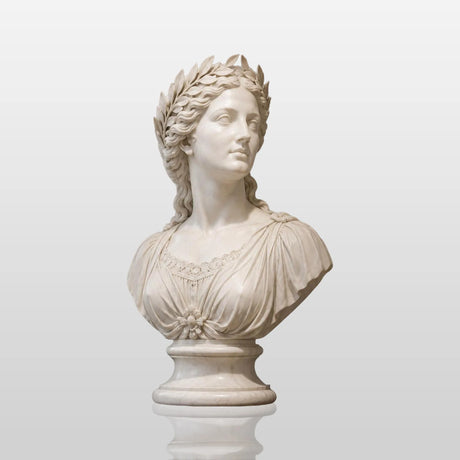 A white classical marble bust statue sits on a dark wooden sideboard beside stacked books and small potted greenery in a soft lit interior room.
