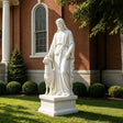 A white marble Good Shepherd statue stands on green grass in front of a brick building.