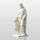 A white marble Good Shepherd statue stands on green grass in front of a brick building.