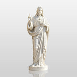 Marble Sacred Heart of Jesus statue stands near a stone church.