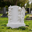 White marble cherub tombstone carved with roses sits on the a green cemetery lawn.
