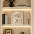 Marble Virgin Mary wall relief sculpture displayed on lit built in shelving indoors.
