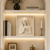 Marble Virgin Mary wall relief sculpture displayed on lit built in shelving indoors.