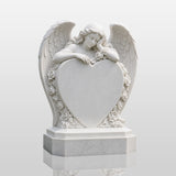 White marble tombstone carved with angel, roses and central blank heart stands on the black gravel cemetery ground.